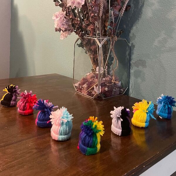 A set of 8 Pride hats, with an ornament dedicated to each pride flag: rainbow, lesbian, gay, bisexual, pansexual, transgender, non-binary, and asexual. All handcrafted by Nerdfighter Alex