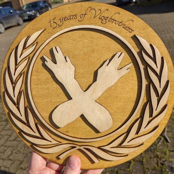 Celebrate 15 years of Vlogbrothers with a Nerdfighter crest wooden plaque made by nerdfighter Jim Adkins. (Measures 8.4x8.8 inches)